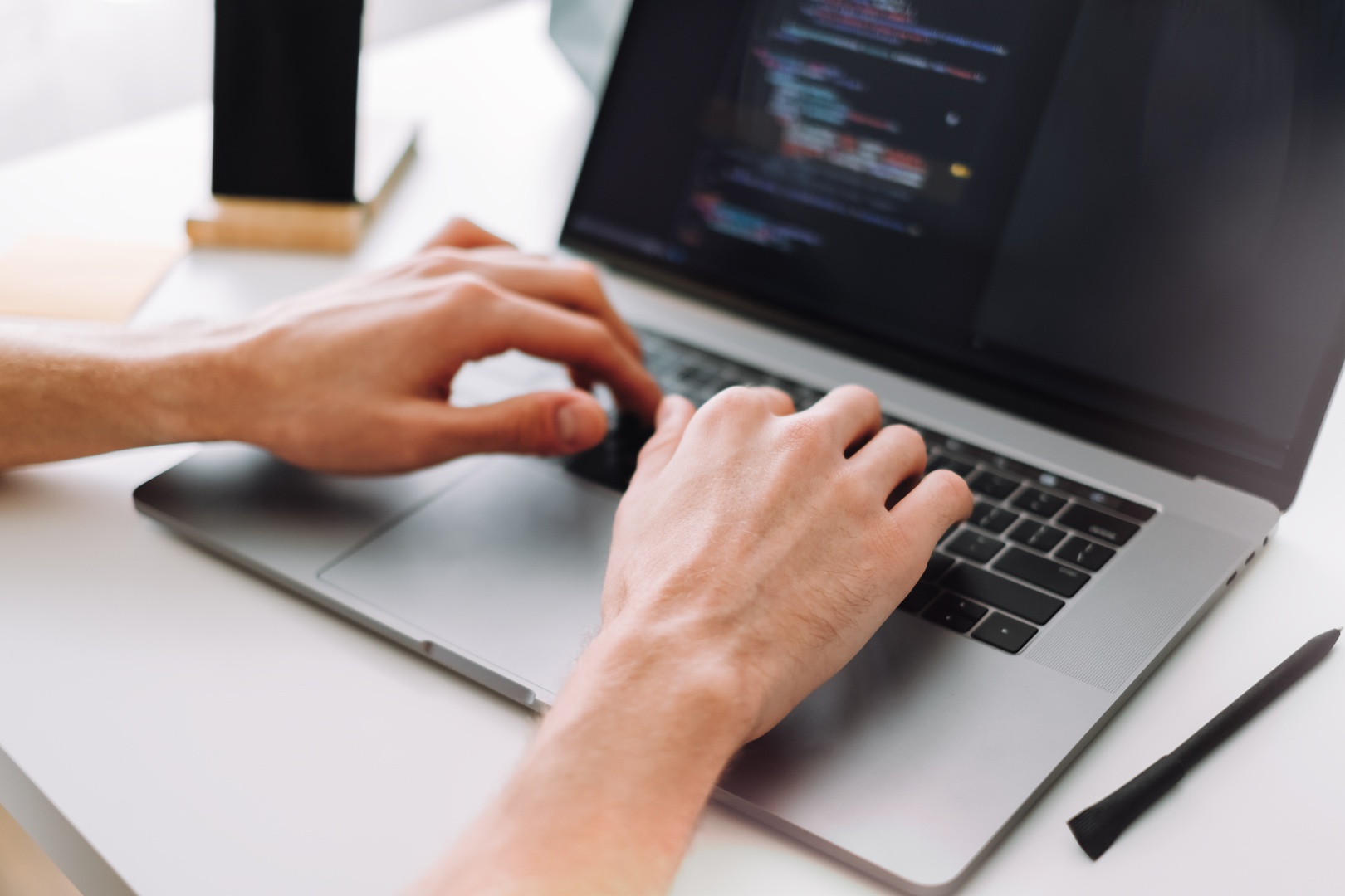 Hands typing on a laptop with a screen showing software code, illustrating best practices for software management and TRaViS ASM solutions.