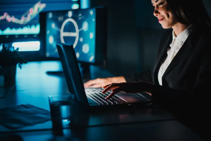 Professional woman working on a laptop with cybersecurity graphics and outdated software vulnerabilities highlighted on a digital display.