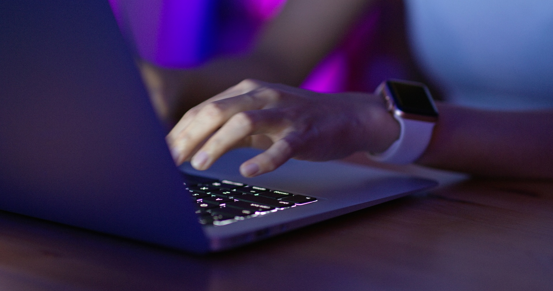  Person working on a laptop in a dimly lit environment with a futuristic purple and blue glow, representing AI-driven cybersecurity and predictive threat modeling.