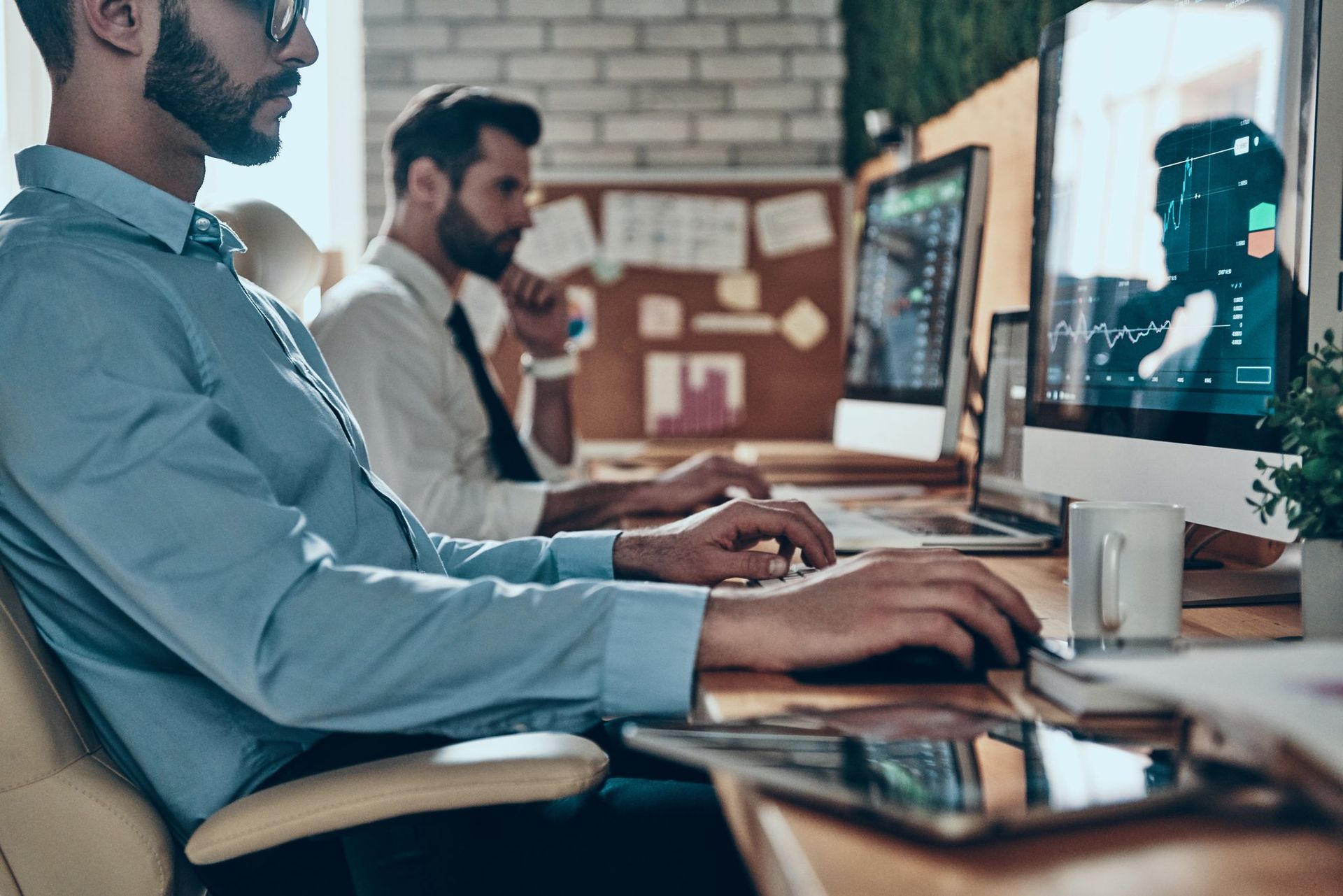 Image of two men at computers thinking about using travisasm to implement a proactive dark web breach prevention program.