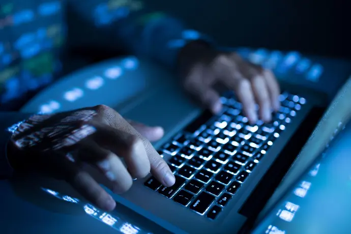 Image showing two human hands on a laptop securing digital assets in the dark.