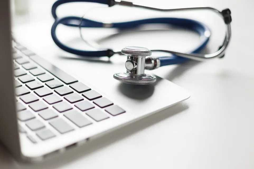 Picture of laptop with blue stethescope on a table.