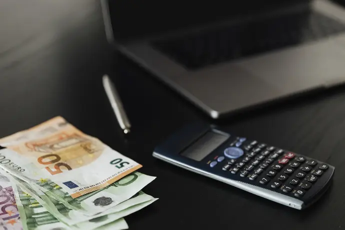 Image of a laptop on a desk in a financial institution next to a calculator and money.